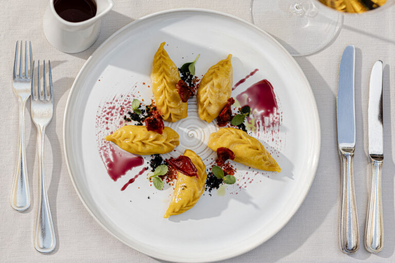 Sechs gelbe Dessert-Quenelles auf wei&szlig;em Teller mit roten Saucenstrichen, Beeren und Kr&auml;uter, serviert im Hotel Haus am Hang.