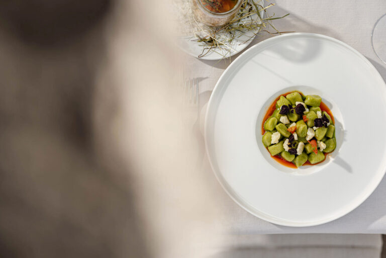 Wei&szlig;e Platte mit kleinem Turm aus gew&uuml;rfeltem Gem&uuml;se und Kr&auml;utern; oben rechts Glas mit Getr&auml;nk; linker Bereich unscharf