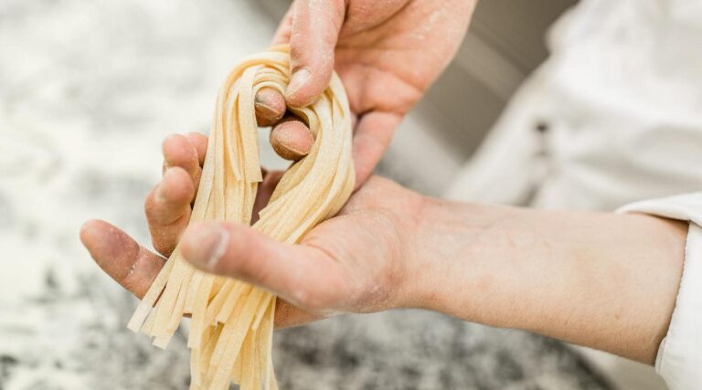 Zwei H&auml;nde formen frische Bandnudeln aus Teig in einer Hotelk&uuml;che
