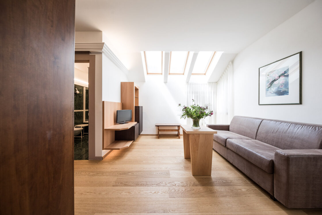 Helle Suite unter Dach mit Sofa, Holzfußboden, niedriger Tisch mit Blumen, Wandregal mit TV und drei Dachfenstern