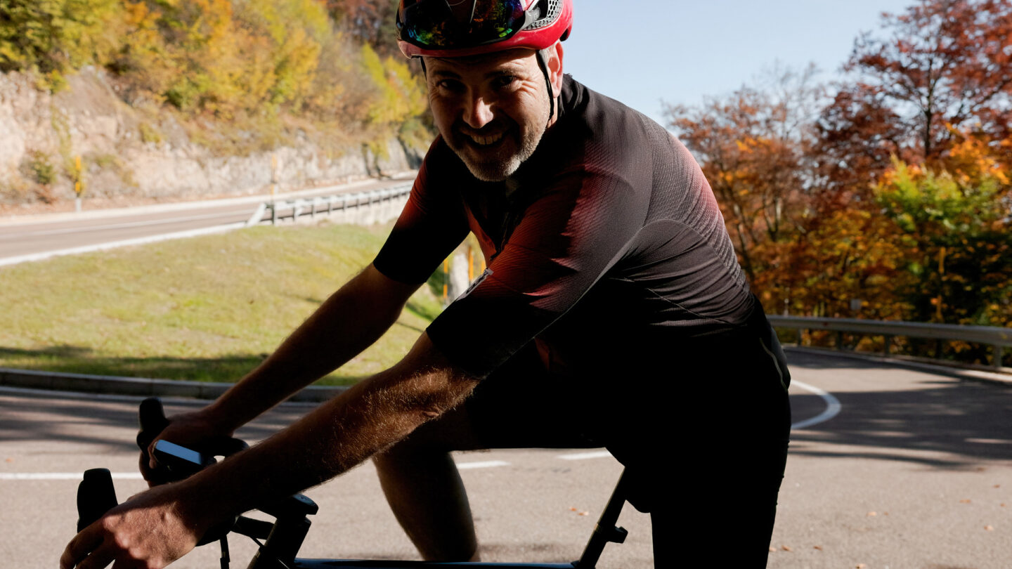 Radfahrer mit Helm im Schatten an Lenker, hinter ihm Holzzaun und herbstliche Bäume; Fahrradurlaub in Kaltern.