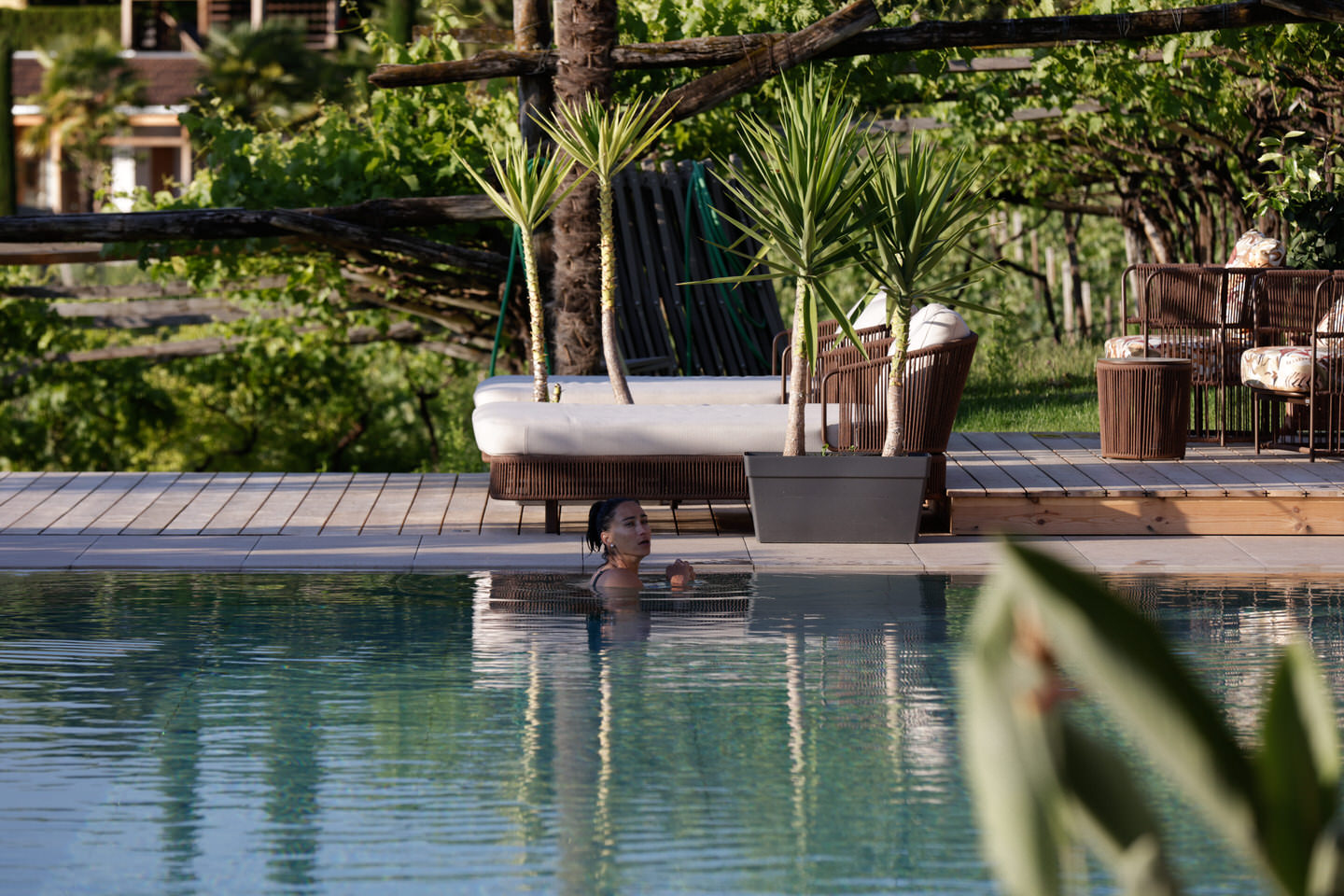 Tagesbett mit Kissen und Decke auf Holzdeck am ruhigen Wasser, umgeben von Palmen und Uferbepflanzung