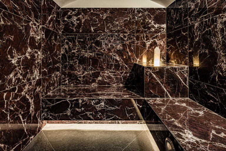 Dunkle, gl&auml;nzende Marmorw&auml;nde mit eingelassener Ablage, drei brennende Kerzen und indirekte Bodenbeleuchtung